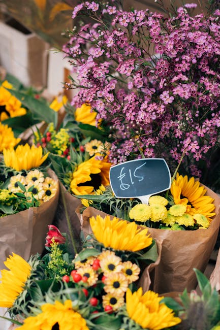 A vibrant floral display at Stamford Hill florist, featuring freshly arranged bouquets with bright yellow sunflowers, small white daisies, and red accents, all wrapped in brown paper. Behind these, a